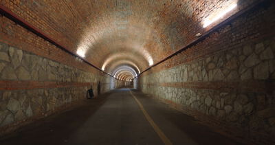 Langer Tunnelgang mit Natursteinmauern unter beleuchtetem Ziegelgewölbe, Tunnelinneres, im Tunnel und Tonnengewölbe als 4K