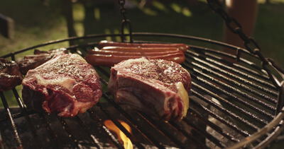 Gewürzte Steaks und Würstchen garen auf dem Schwenkgrill über offener Flamme