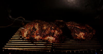 Großer gewürzter Braten ruht auf dem Grillrost im dunklen Ambiente