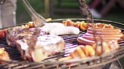 Steak und Würste brutzeln auf dem Schwenkgrill im Garten