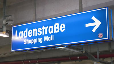Blaues Hinweisschild zur Ladenstraße mit weißem Richtungspfeil