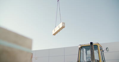 Kran hebt ein verpacktes Baustoffpaket vor hellem Himmel empor