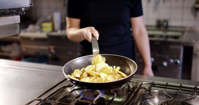 Koch brät goldene Kartoffelscheiben in der Pfanne über offener Gasflamme