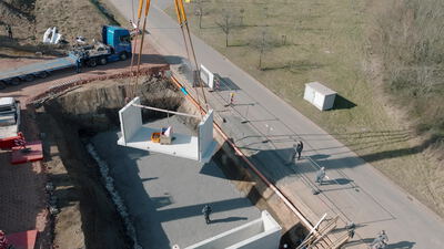 Mobilkran hebt Betonfertigteil in Baugrube neben der Straße