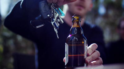 Mann öffnet eine braune Bierflasche mit einem Schlüssel, Flasche öffnen, Bügelflasche und draußen als 4K Stockvideo