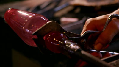 Glasbläser formt glühendes rotes Glas mit einem Handwerkzeug