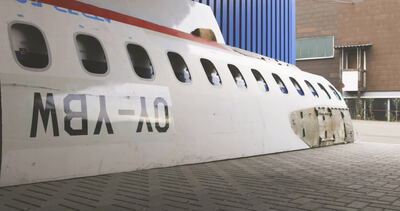 Ausrangierter Flugzeugrumpf steht vor einer blauen Industriehalle