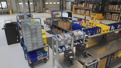 Kommissionierung im Lager an einer modernen Verpackstation Kommissionierung im Lager an einer modernen Verpackstation, Kommissionierwagen, Intralogistik und Lagerhalle als 4K