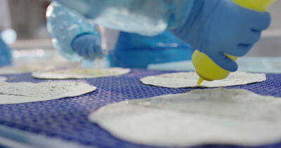 Dosierflasche füllt Sauce auf Teigfladen in der Snackproduktion