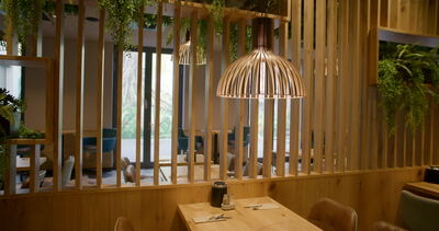 Kamerafahrt entlang Holzlamellenwand mit Korblampe im Restaurant zeigt gedeckte Tische