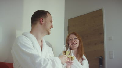 Paar im Bademantel stößt mit Weißwein im Wellnesshotel an