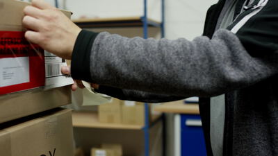 Mitarbeiter klebt eine Versandtasche auf einen Karton im Lager