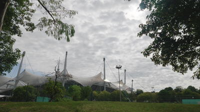 Zeltdach des Olympiaparks liegt hinter einer weiten Wiese im Grünen: Olympiapark, Zeltdach Weitblick