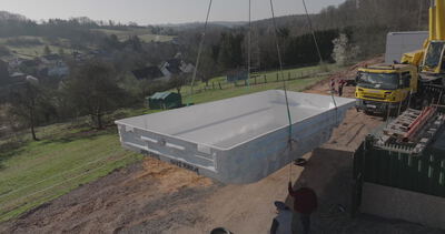 Kran hebt weißes Schwimmbecken in eine Baugrube