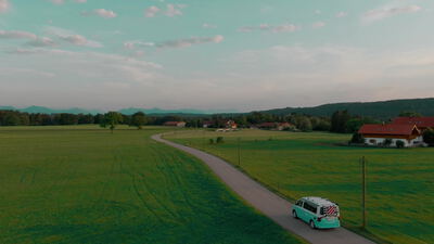 Ein türkisfarbener Kleinbus fährt aus der Vogelperspektive über eine Landstraße