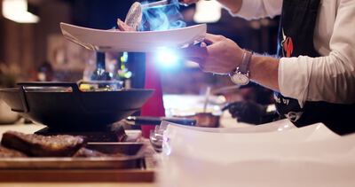 Koch serviert ein Steak auf weißem Teller mit blauer Flamme am Tisch
