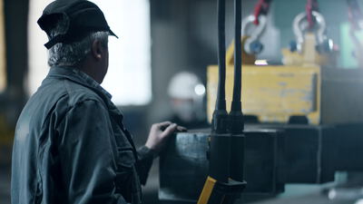 Arbeiter bearbeitet Metallblock unter einem Lastmagneten in der Schwerindustrie