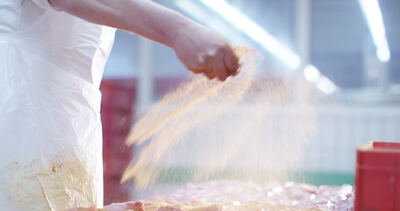 Ein Metzger streut schwungvoll Gewürze über frisches Fleisch