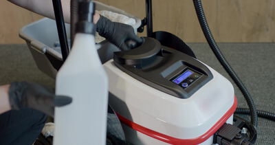 Behandschuhte Hand bedient das Bedienfeld eines Dampfreinigers mit blauer LED Anzeige