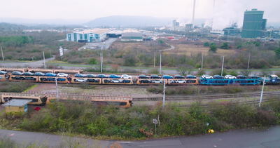 Autotransportzug mit neuen Fahrzeugen vor einem Stahlwerk