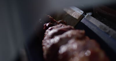Dunkel gewürztes Fleisch liegt in Nahaufnahme an der Schneidemaschine