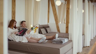 Paar entspannt im Bademantel auf einer Liege im Wellnessbereich
