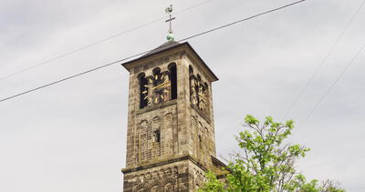 Historischer Kirchturm mit Turmuhr und Kreuz vor bewölktem Himmel