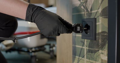 Behandschuhte Hand steckt das Stromkabel eines Dampfreinigers in eine Wandsteckdose: Stromkabel einstecken, Wandsteckdose