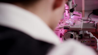 Laborant arbeitet an einem Präzisionsgerät im rosa beleuchteten Labor