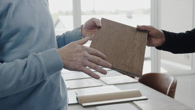 Zwei Personen begutachten ein Holzmuster am Tisch im Büro