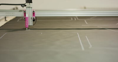 Flachbettplotter zeichnet Schnittmuster auf graues Material Flachbettplotter zeichnet Schnittmuster auf graues Material, Schnittmuster zeichnen, Umrisse auf Stoff und verschachtelte