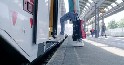 Fahrgast steigt mit Tragetasche in den Zug am Bahnsteig