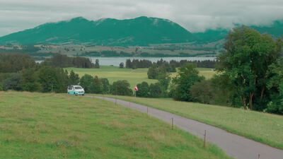 Campingbus fährt durch die grüne Alpenlandschaft am See