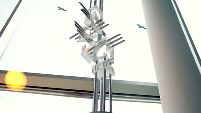Abstrakte Glasskulptur vor heller Fassade mit Flugzeug am Himmel, abstrakte Skulptur, Kristallskulptur und Kunst am Bau als