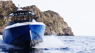 Blaues Schnellboot rast mit Gischt an einer Felsklippe vorbei