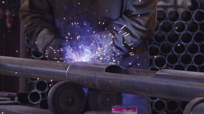 Schweißer verbindet zwei Stahlrohre mit funkensprühender Nahtschweißung in der Metallwerkstatt