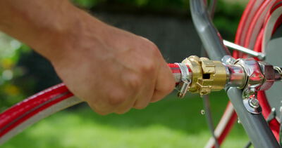 Hand steckt roten Gartenschlauch auf Schlauchwagen im Garten