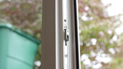 Metallbeschlag an einem gekippten Fenster mit Blick in den grünen Garten