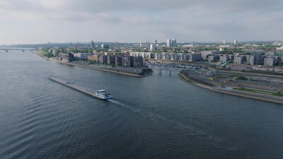 Frachtschiff durchquert breiten Fluss vor moderner Stadtkulisse