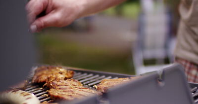 Hand wendet Fleisch mit der Grillzange auf dem Grill