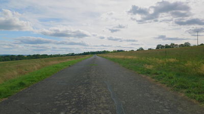 Schmale Landstraße mit rissigem Asphalt zwischen weiten Feldern, schmale Straße, rissiger Asphalt und geflickter Asphalt als
