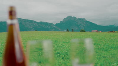 Bierflasche und Gläser auf einer Almwiese vor Bergpanorama