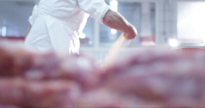 Metzger arbeitet in einer hellen Fleischerei mit rohem Fleisch im Vordergrund
