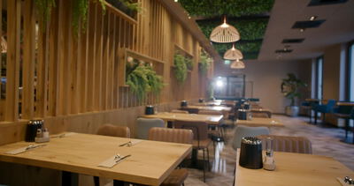 Restauranttische stehen vor grüner Pflanzenwand unter warmen Holzleuchten: Restaurant Pflanzenwand, grüne Wand im Restaurant