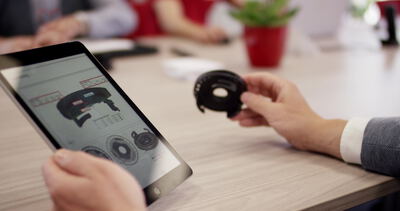 Hände präsentieren ein Gummiteil mit Tablet in einer Besprechung