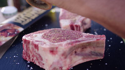 Rohes Steak am Knochen wird mit frisch gemahlenem Pfeffer gewürzt