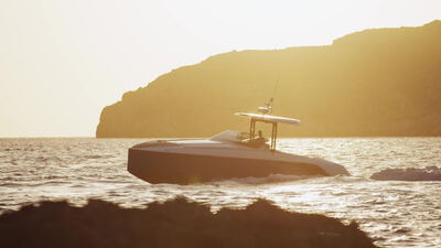 Luxuriöses Sportboot gleitet bei goldenem Abendlicht an einer Landzunge vorbei