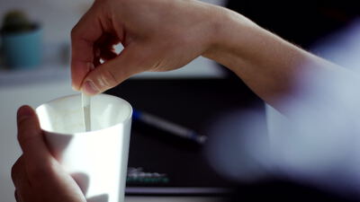 Hände tauchen einen Teebeutel in eine weiße Tasse