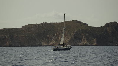 Segelyacht faehrt vor einer felsigen Kueste ueber das Meer