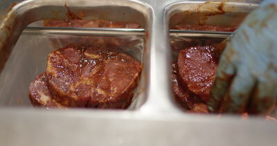Marinierte Steaks in roter Würzsoße liegen in Edelstahlbehältern: marinierte Steaks, Marinade